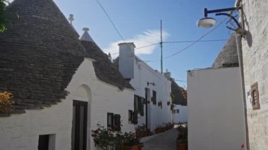 Alberobello, İtalya 'da güzel bir ara sokak. Berrak gökyüzünün altında eşsiz beyaz trulli evler ve saksıda çiçekler var..