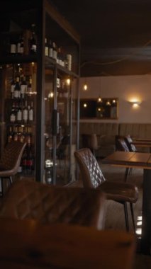 Samimi ışıklandırma, şarap şişeleri, boş masalar ve sakin bir yemek atmosferini tasvir eden rahat oturma alanları olan şık bir restoran..