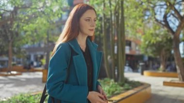 Güneşli bir şehir parkında akıllı telefon kullanan genç bir kadın