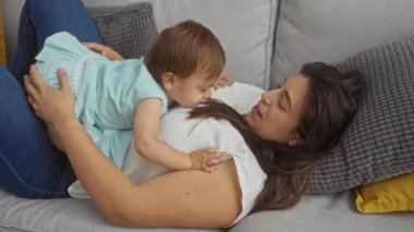 Anne, küçük kızıyla oturma odasında kanepede oynuyor. Evde sevgi ve bağlılık gösteriyor.