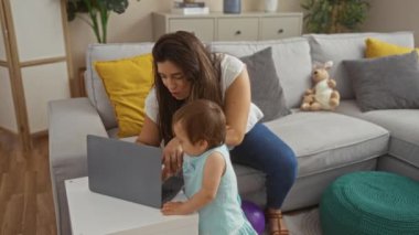 Anne ve kızı evlerinin oturma odasında dizüstü bilgisayar kullanıyor, oyuncaklar ve rahat mobilyalarla çevrili, aile sevgisini somutlaştırıyor ve birbirlerine bağlanıyorlar..