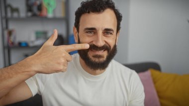 Keyifli orta yaşlı sakallı bir adam rahat bir oturma odasında gülüşünü gösteriyor, pozitiflik ve refahını gösteriyor..