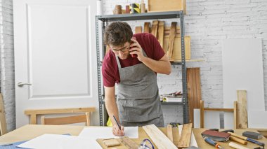 Sakallı genç bir İspanyol, ahşap atölyesinde telefonla konuşurken notlar alıyor..