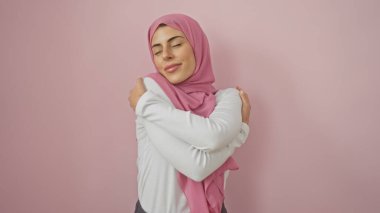 Pembe tesettürlü, dingin genç bir kadın pembe bir arka plana sarılıyor. Kendine güveni ve güveni tam..