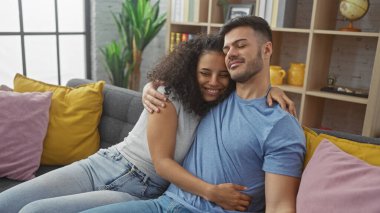 Sevgi dolu bir çift, sıcak bir oturma odasında kanepede sarılıyor, mutluluğu ve birlikteliği yansıtıyor..