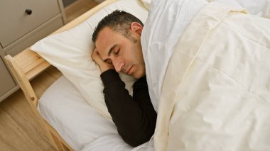 Parlak bir yatak odasında huzur içinde uyuyan bir adam, evde rahatlık ve rahatlık tasvir eder..