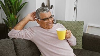 Rahat son sınıf öğrencisi, gözlüklü gülümsüyor, evinde sarı bir kupa tutuyor..