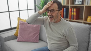 Gözlüklü ve sakallı olgun bir adam. Kapalı bir koltukta oturmuş sürpriz yapıyor.