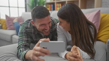Mutlu adam ve kadın evdeki kanepede akıllı telefonuyla bir an paylaşıyorlar..