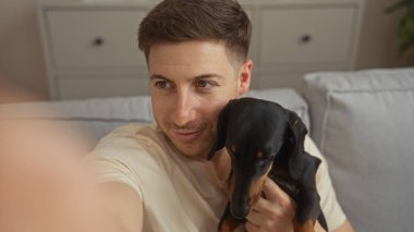 Genç bir İspanyol adam evdeki rahat bir oturma odasında köpeğiyle selfie çekiyor..