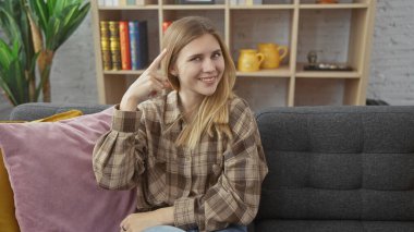 Sarışın genç kadın gülümsüyor ve sıcak bir oturma odasında bir fikir belirtiyor..