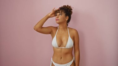 Beyaz bikinili güzel Latin kadın izole edilmiş pembe arka planda rahatça poz veriyor.