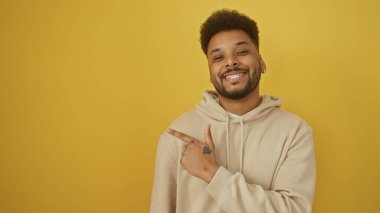 Neşeli bir siyah adam, sarı bir arka planı işaret ederek pozitifliği ve gelişigüzel tarzını gösteriyor..