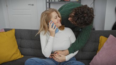 Telefondaki neşeli bir kadın samimi bir oturma odasında sevgi dolu bir adama sarılıyor samimiyeti ve sıcaklığı yansıtıyor..