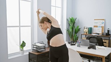 Genç bir kadın modern bir ofis ortamında esneyerek, işyerinde ya da sağlıkta ara verilmesini öneriyor.