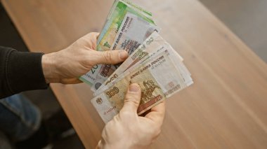 Bir adamın elleri kapalı alanda bulanık bir arkaplanda Rus rublesini tutuyor..