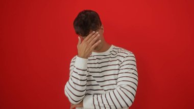 Yakışıklı, genç, İspanyol bir adam, portrede, izole edilmiş, koyu kırmızı bir arka plana karşı hayal kırıklığını dile getiriyor..