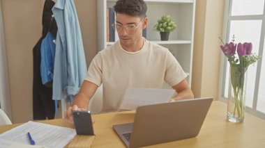 Yakışıklı bir İspanyol evdeki bilgisayarlı ve akıllı telefonlu belgeyi incelerken pencere kenarındaki çiçekli ahşap bir masada..