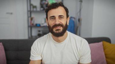 Modern bir oturma odasında gülümseyen sakallı orta yaşlı bir adam.