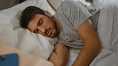 Yakışıklı, sakallı, genç bir adam. Yatak odasında huzur içinde uyuyor..
