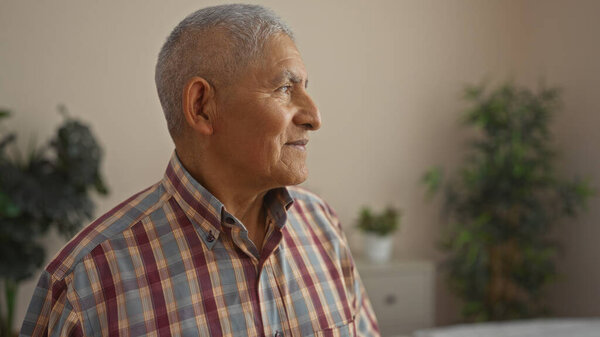 Elderly hispanic man with grey hair looking sidewards, indoors in a homey living room.
