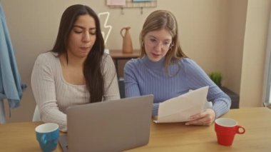 Evde dizüstü bilgisayarı, mavi ve kırmızı bardakları, dokümanları, gözlükleri olan, günlük kıyafetleri olan iki kadın iş birliği yapıyor..