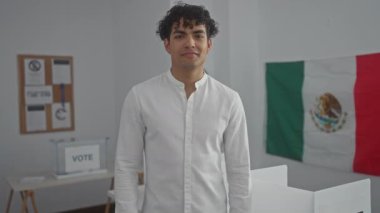 Neşeli bir İspanyol adam Meksika 'da bir seçim merkezinde arka planda bir bayrak ile kamerayı işaret ediyor..