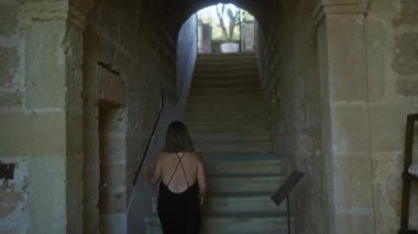 İtalyan masserisiyle taştan bir merdivenden çıkan bir kadın, güneşli bir kaktüse giden kapalı kemer yolu, sakin ve tarihsel bir atmosfer yaratıyor..