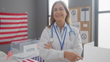 Gülümseyen kadın, bayrak, oy sandığı ve oy kullanma gereçleri olan bir odada Amerikan seçimleri sırasında parmakla işaret ediyor..