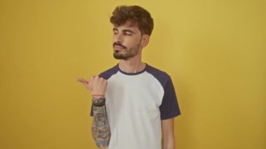 Mutlu İspanyol genç adam neşeyle işaret ediyor ve bakıyor, canlı sarı arka planda, bulaşıcı bir tebessümle tek başına duruyor.