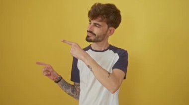 İki eli yanda duran genç İspanyol adam, kameraya gülümsüyor, sarı arka planda izole edilmiş.