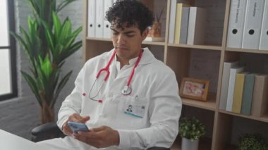 Genç bir İspanyol erkek doktor, bir klinikteki akıllı telefondan hastanın tıbbi kayıtlarını inceliyor..