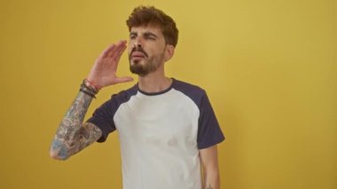 Hislerini ifade eden, ayakta duran, yüksek sesle bağıran, yandan bağıran genç bir İspanyol; izole edilmiş sarı arka plan üzerinde canlı bir iletişim anı