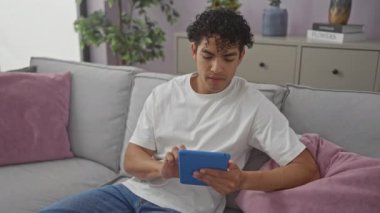 Beyaz gömlekli İspanyol adam oturma odasındaki kanepede tablet kullanıyor.