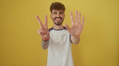 Neşeli genç İspanyol adam, kendine güvenerek ayakta duruyor ve gülümsüyor, 7 numarayı parmaklarıyla gösteriyor, mutlu, işaret ediyor, izole edilmiş sarı arka planda.