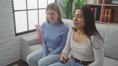 Kanepede oturan iki kadın, biri sıcak bir oturma odasında uzaktan kumandayı tutarken, mutlu bir şekilde bir anı paylaşıyorlar..