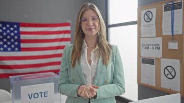 Kendine güvenen genç bir kadın, Amerikan bayrağı arkaplanında seçim katılımını somutlaştıran bir Amerikan oy kullanma merkezindeki kameraya işaret ediyor..