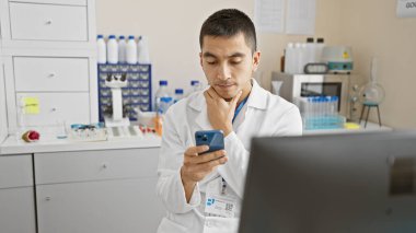 Laboratuvar ortamında akıllı telefon kullanan labaratuvar önlüklü İspanyol bir adam..