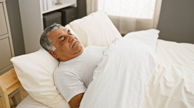 Olgun bir adam, modern bir yatak odasında tek başına uyur. Evinde rahatlığını sergiler..