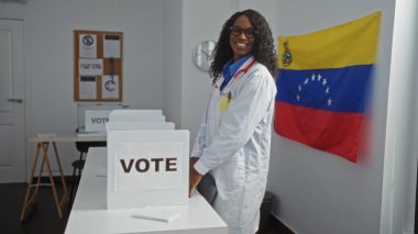 Kıvırcık saçlı, güzel bir Afro-Amerikalı kadın oy kabinlerinde gülümseyen Venezuela bayrağıyla seçim odasında duruyor..