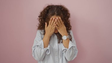 Pembe bir duvara yaslanmış bir kadın yüzünü kapatıyor.