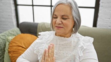Beyaz giyinmiş olgun bir kadın, gözleri kapalı bir şekilde evdeki kanepeye uzanmış, dinginlik ve sükunet saçan..