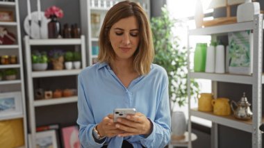 Ev dekorasyonu mağazasında akıllı telefon kullanan genç bir kadın çeşitli dekorasyon ve bitkilerle çevrili, şık bir iç mekan yaratıyor.