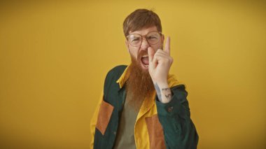 Öfkeli, sakallı, kızıl saçlı bir adam sarı bir arka plana el sallıyor. Duygularını yansıtıyor..