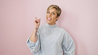 Kısa sarı saçlı neşeli bir İspanyol kadın pembe bir duvara poz veriyor, kendine güveni ve mutluluğu yayıyor..