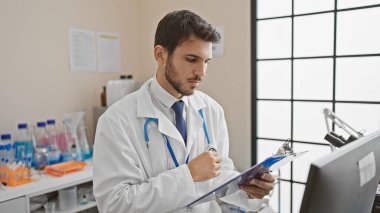 Beyaz laboratuvar önlüklü odaklanmış genç bir Latin, parlak ışıklandırılmış hastane laboratuarındaki belgeleri inceliyor..