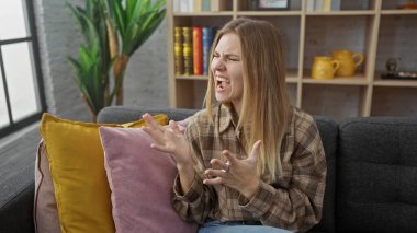 Genç sarışın bir kadın, renkli yastıklarla çevrili bir kanepede otururken hayal kırıklığını ifade eder..