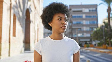 Şık bir Afro-Amerikan kadını doğal kıvırcık saç stiliyle şehir ortamında poz veriyor..