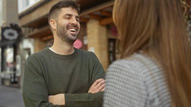 Güler yüzlü bir adam güneşli bir şehir sokağında bir kadınla sohbet ediyor, aşkı ve açık hava ilişkisini çağrıştırıyor.