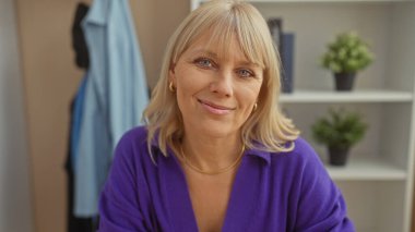 Kapalı bir ortamda sarı saçlı, gülümseyen beyaz bir kadının portresi, büyüleyici ve nazik bir özgüven..